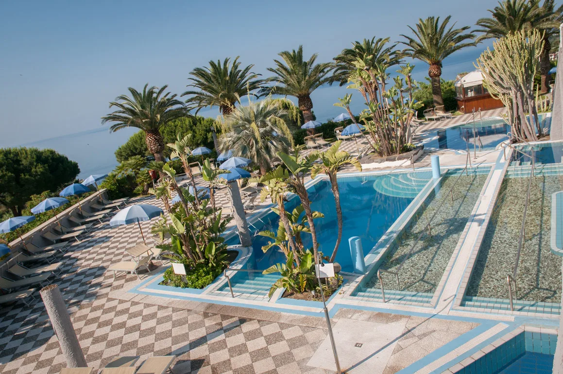 Vista dall'alto delle piscine termali con palme e ombrelloni azzurri
